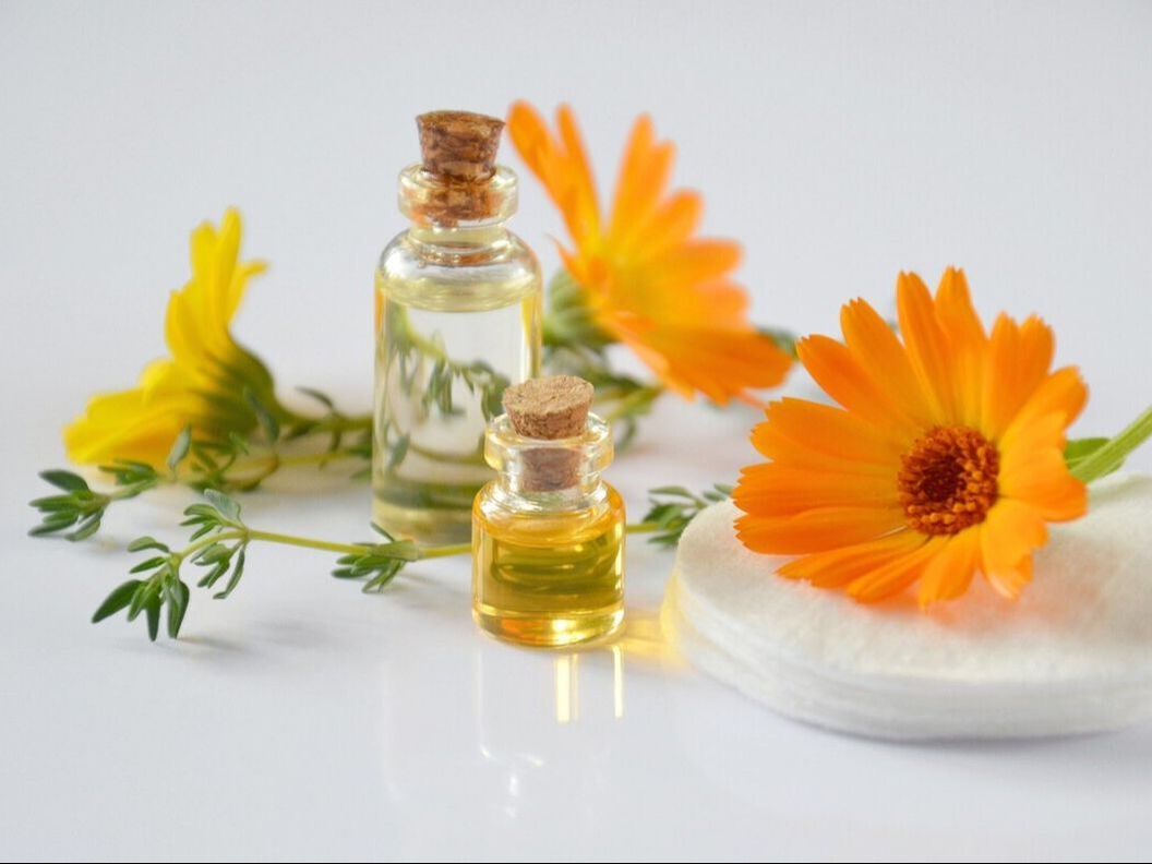 Two vials of perfume in front of orange and yellow flowers to demonstrate the types of product photos you learn to take in this photography class