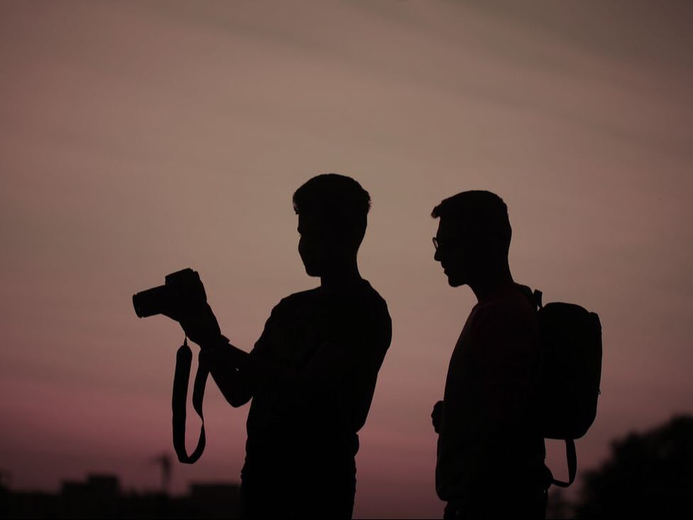 Two people, one person showing the other how to use a camera with a sunset behind them, used to demonstrate the private nature of our photography lessons